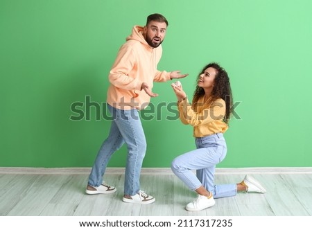 Young woman proposing to her shocked boyfriend on color background Royalty-Free Stock Photo #2117317235