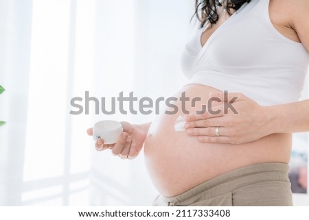 young pregnant woman applies cream on her tummy to keep skin moisturized. prevention of stretch marks in pregnancy. health and body care concept Royalty-Free Stock Photo #2117333408