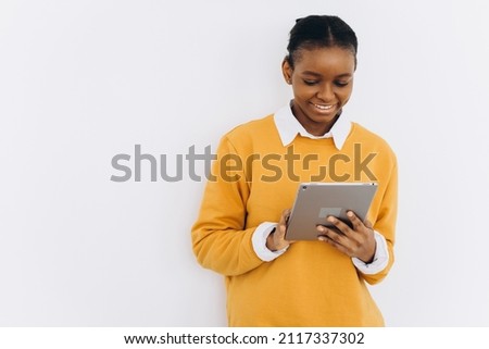Happy black student girl in a yellow jacket holds a tablet and shows cheers on a white background
