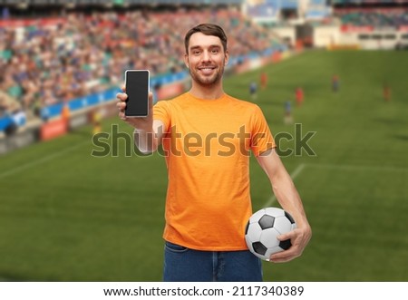 sport, leisure games and online betting concept - happy smiling man or football fan with smartphone and soccer ball over stadium background Royalty-Free Stock Photo #2117340389