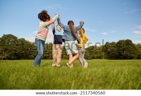 childhood, leisure and people concept - group of happy kids playing round dance at park Royalty-Free Stock Photo #2117340560
