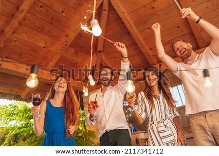 Group of cheerful young friends having fun dancing and drinking cocktails at birthday party