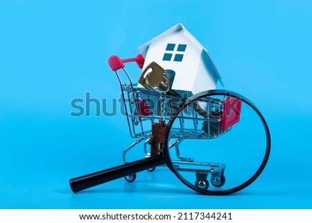 Toy model house, magnifying glass,money and keys in a shopping cart.
