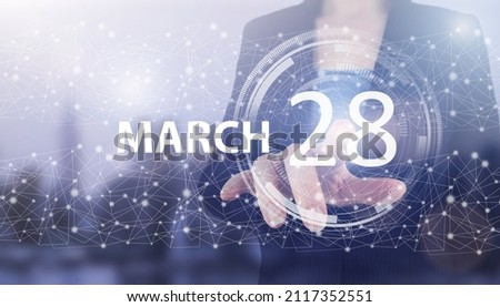 March 28th. Day 28 of month, Calendar date. Hand click luminous hologram calendar date on light blue town background. Spring month, day of the year concept