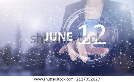 June 12nd. Day 12 of month, Calendar date. Hand click luminous hologram calendar date on light blue town background. Summer month, day of the year concept