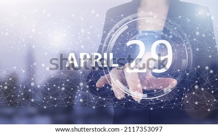 April 29th. Day 29 of month, Calendar date. Hand click luminous hologram calendar date on light blue town background. Spring month, day of the year concept