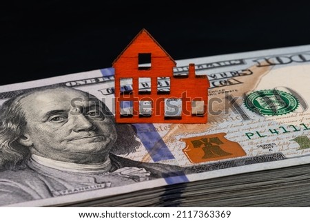 Wooden symbolic house and 100 American dollars on a black background