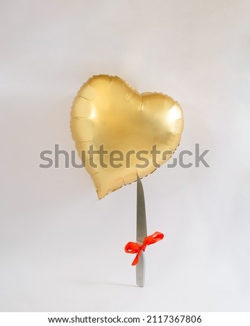 Heart balloon gold flying . Knife with red ribbon waiting to poke the heart. Valentine love danger concept idea.