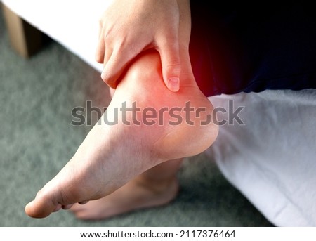 A person holding ankle on Achilles tendon, suffering with pain in red spot area. Sprain ligament or Achilles tendonitis symptoms. Image with red highlights on hurting area, Health care concept Royalty-Free Stock Photo #2117376464