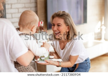 Portrait of blond woman mother celebrating and congratulating happy birthday party, presenting cake to infant in hands, decorated by bears cartoons. Baby back. Indoor apartment. Delightful family.