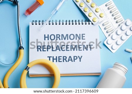 Notebook with text Hormone Replacement Therapy and medications on light blue background, flat lay Royalty-Free Stock Photo #2117396609