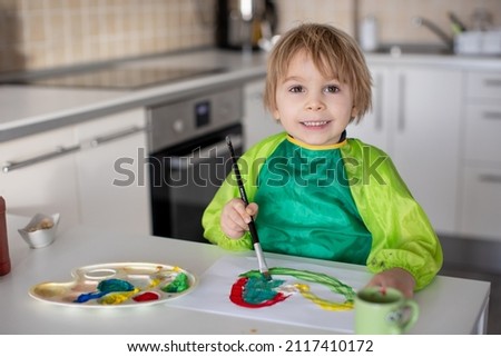 Cute blond boy, preschool child, painting at home with aquarelle colors card for Valentine