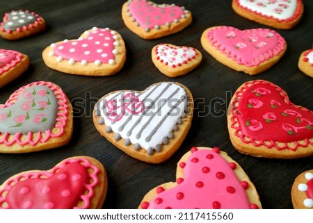 Heap of beautiful heart shaped with lovely pattern cookies scattered on black wooden backdrop