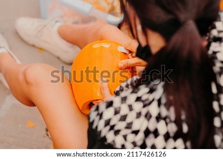 Young woman wearing Halloween costume making decoration from orange pumpkin. Celebrating Happy Halloween