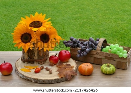 A bouquet of sunflowers with grapes, apples and pumpkins on a table in the garden.