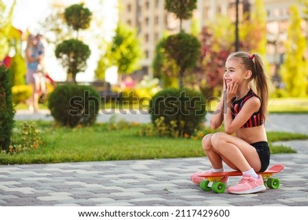 european girl of school age in short black shorts and a pink top  riding a skateboard at summer park 