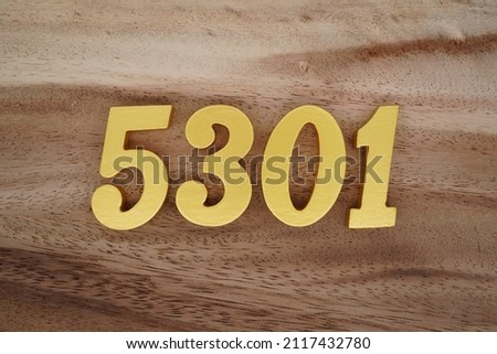 Wooden Arabic numerals 5301 painted in gold on a dark brown and white patterned plank background.