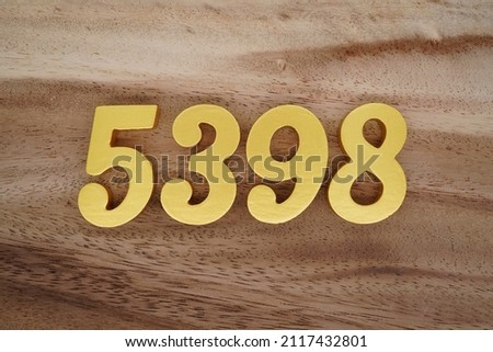 Wooden Arabic numerals 5398 painted in gold on a dark brown and white patterned plank background.