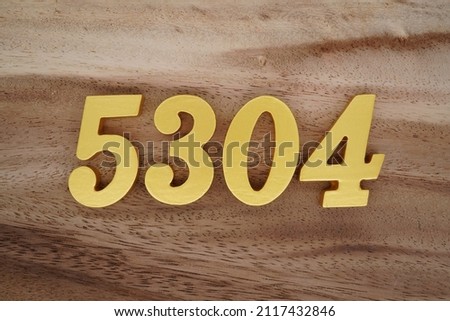Wooden Arabic numerals 5304 painted in gold on a dark brown and white patterned plank background.