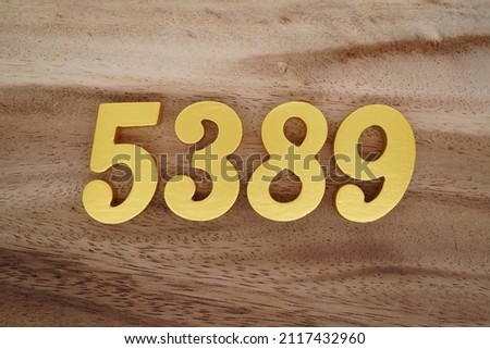 Wooden Arabic numerals 5389 painted in gold on a dark brown and white patterned plank background.
