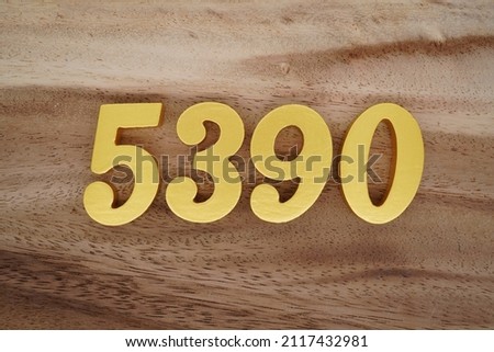 Wooden Arabic numerals 5390 painted in gold on a dark brown and white patterned plank background.