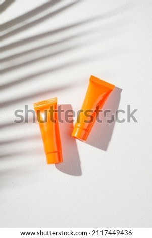Plastic orange bottles for cream or lotion on a white background. Skin care cosmetic with beautiful palm shadows. Beauty concept for face body care. Place for text