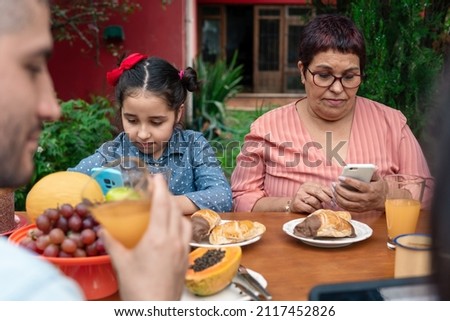 brazilian granny using mobile and having breakfast outside in the garden