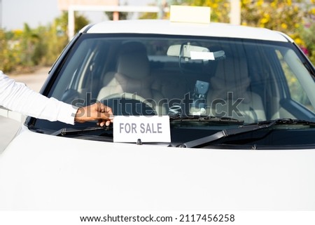 Close up shot of owner placing car for sale sign board in front of car - concept of business loss, personal probleams, financial criss, bankrupt and debt.