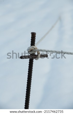 t shaped cross shaped metal rebar post with rope tied in knot around top for support for fenced off safety area in winter vertical format room for type white background religious symbol religion tied 