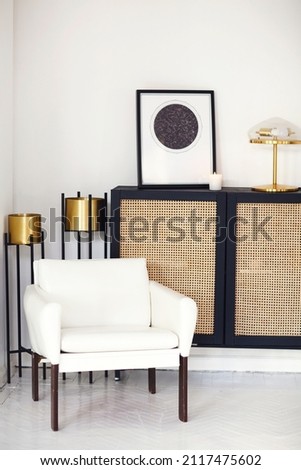 Black wooden commode or dresser with framed star map poster, lamp and candle against light wall in minimalist contemporary room interior. Interior design elements, furniture and homewares