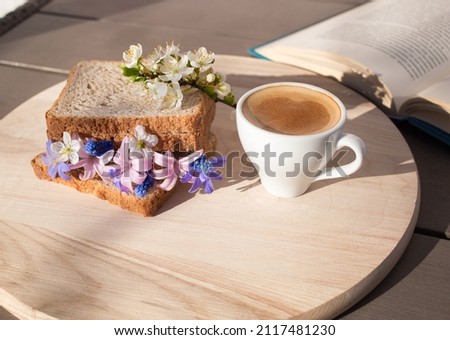sandwich with spring flowers between slices of toast, a cup of coffee and a book is a wonderful healthy breakfast. good morning, flower fantasies, positive atmosphere, flora inspiration. Hi spring