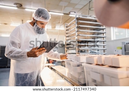 A food factory supervisor using tablet and assesses quality of food. Royalty-Free Stock Photo #2117497340