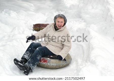 Mature woman young at heart. Happy smiling elderly female riding on snow tubing. Senior lady sledding slide down hill. Winter fun activity outdoor. 
