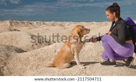 woman with backpack sitting on yellow dunes with dog labrador retriever and hold him by the paw on sunny day Royalty-Free Stock Photo #2117504711