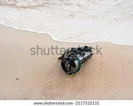 Diver's equipment on sea coast. Rubber flippers and diver propulsion vehicle. Black underwater scooter or swimmer delivery vehicle on sandy beach near sea surf.  Royalty-Free Stock Photo #2117522132