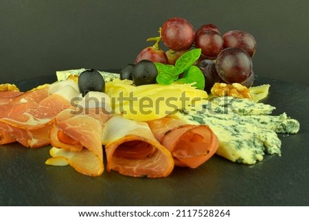 Tray with Schwarzwald ham, cheeses, walnuts, black olives. Decorated with basil. Food on slate backgroud. Copy space