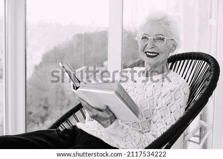 Senior stylish woman sitting on terrace reading book. Education, hobby concept