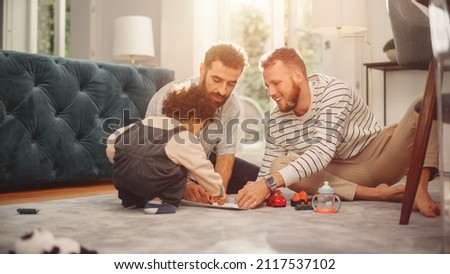 Loving LGBTQ Family Playing with Toys with Adorable Baby Boy at Home on Living Room Floor. Cheerful Gay Couple Nurturing a Child. Concept of Diverse Childhood, New Life, Parenthood. Royalty-Free Stock Photo #2117537102