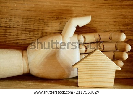 wooden human hand protects Wooden house on wood board background. Eco house