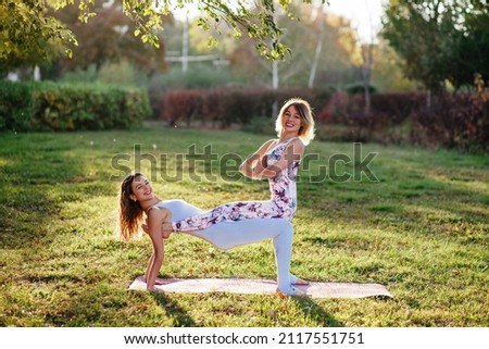 Two women practice yoga in nature perform vrikshasana exercise, tree pose