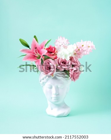 Collage with plaster antique sculpture of human face in a popart style. Creative concept colorful neon ancient statue head, hair made of fresh flowers. Cyberpunk poster on pastel mint background. Royalty-Free Stock Photo #2117552003