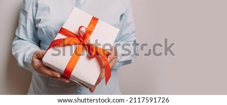 Cropped photo of business woman hands holding paper gift box on gray background. Christmas, new year, birthday concept. Banner, copy space.
