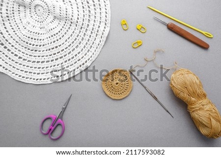 The process of knitting napkins. Photo on a gray background. Openwork napkins of different sizes with a hook for knitting, scissors and a skein of yarn. The concept of creating a product that is part 
