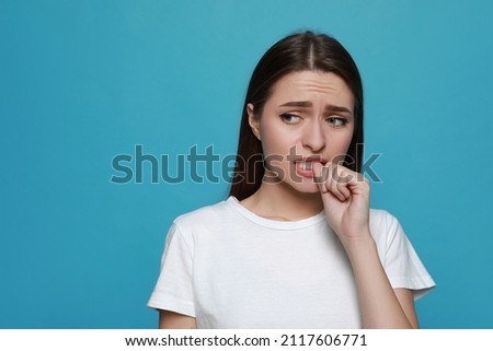 Young woman biting her nails on light blue background. Space for text Royalty-Free Stock Photo #2117606771