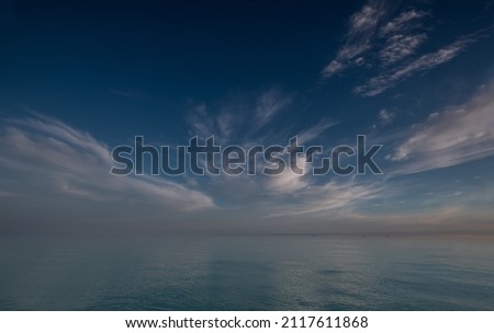 wide angle shot of smooth mirror ocean with light clouds on horizon