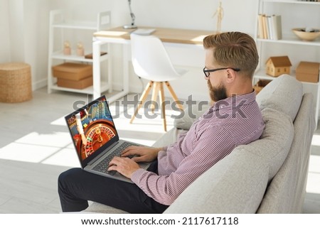 Young man sit relax on sofa play casino online on computer. Caucasian male rest at home couch gamble internet on laptop. Entertainment on web. Gambler or gamer Russian roulette. Royalty-Free Stock Photo #2117617118
