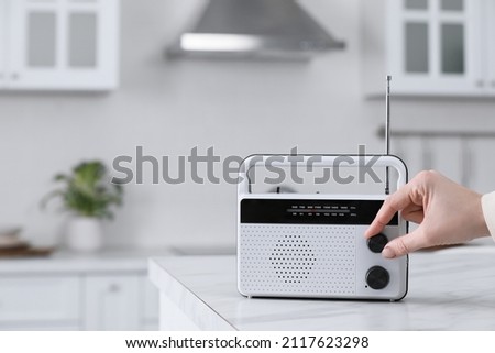 Woman turning volume knob on radio in kitchen, closeup. Space for text Royalty-Free Stock Photo #2117623298