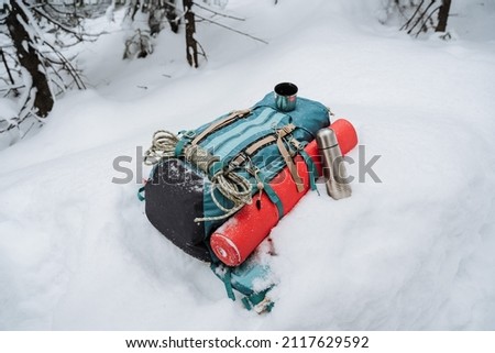 A backpack with camping gear lies on the snow. Winter hike in the mountains, equipment for climbing. Thermos with tea. High quality photo