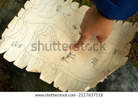 A child's hand points to the place where the treasures are buried. Active games for children. In search of a pirate treasure. Treasure map. Royalty-Free Stock Photo #2117637518