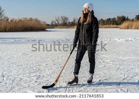 Woman in skates with hockey stick on frozen lake